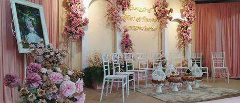 Un escenario con decoración floral, sillas blancas y un cuadro enmarcado.
