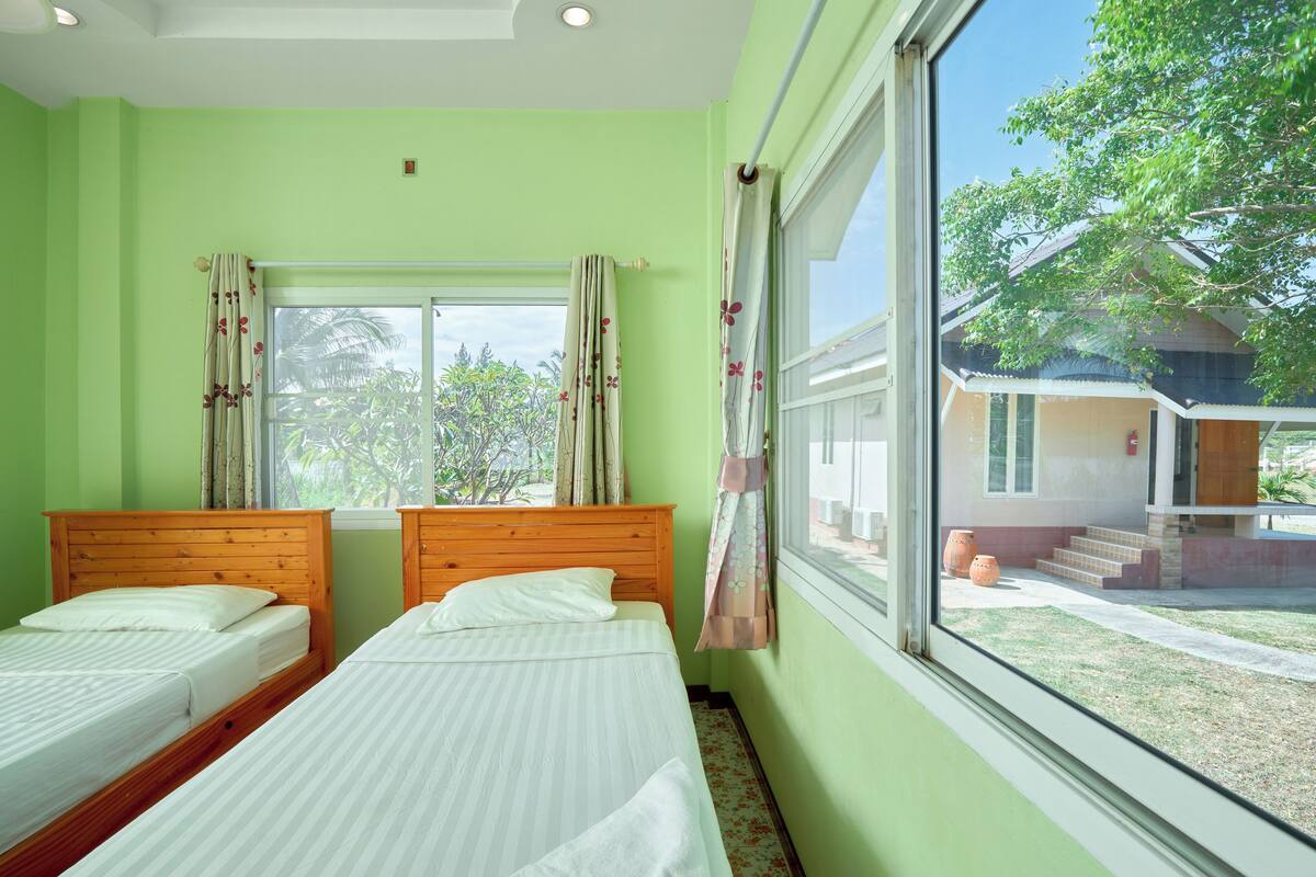 A room with two beds, a large window, and a view of a building outside.