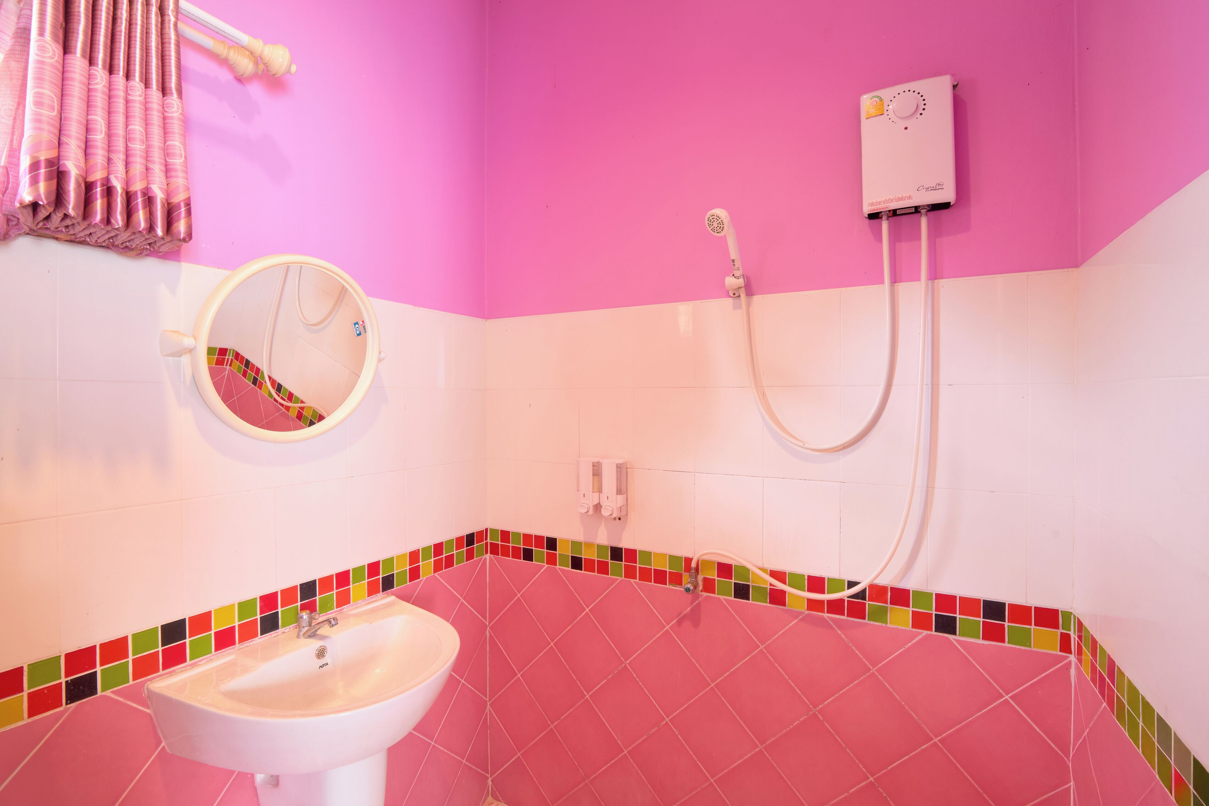 A bathroom with a pink sink, a mirror, and a shower with a handheld showerhead.