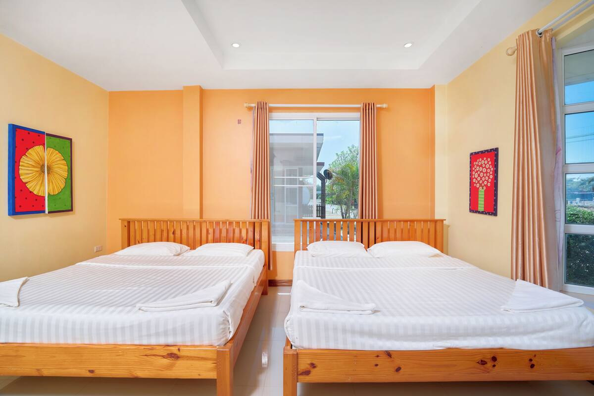 A hotel room with two wooden beds, a large window with curtains, and artwork on the walls.