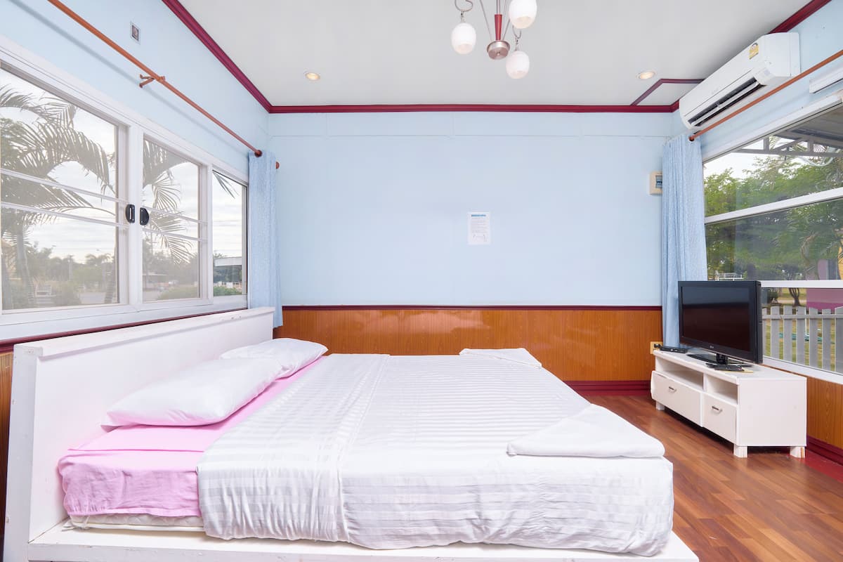A bedroom with a bed, a television, and a window with a view of palm trees.