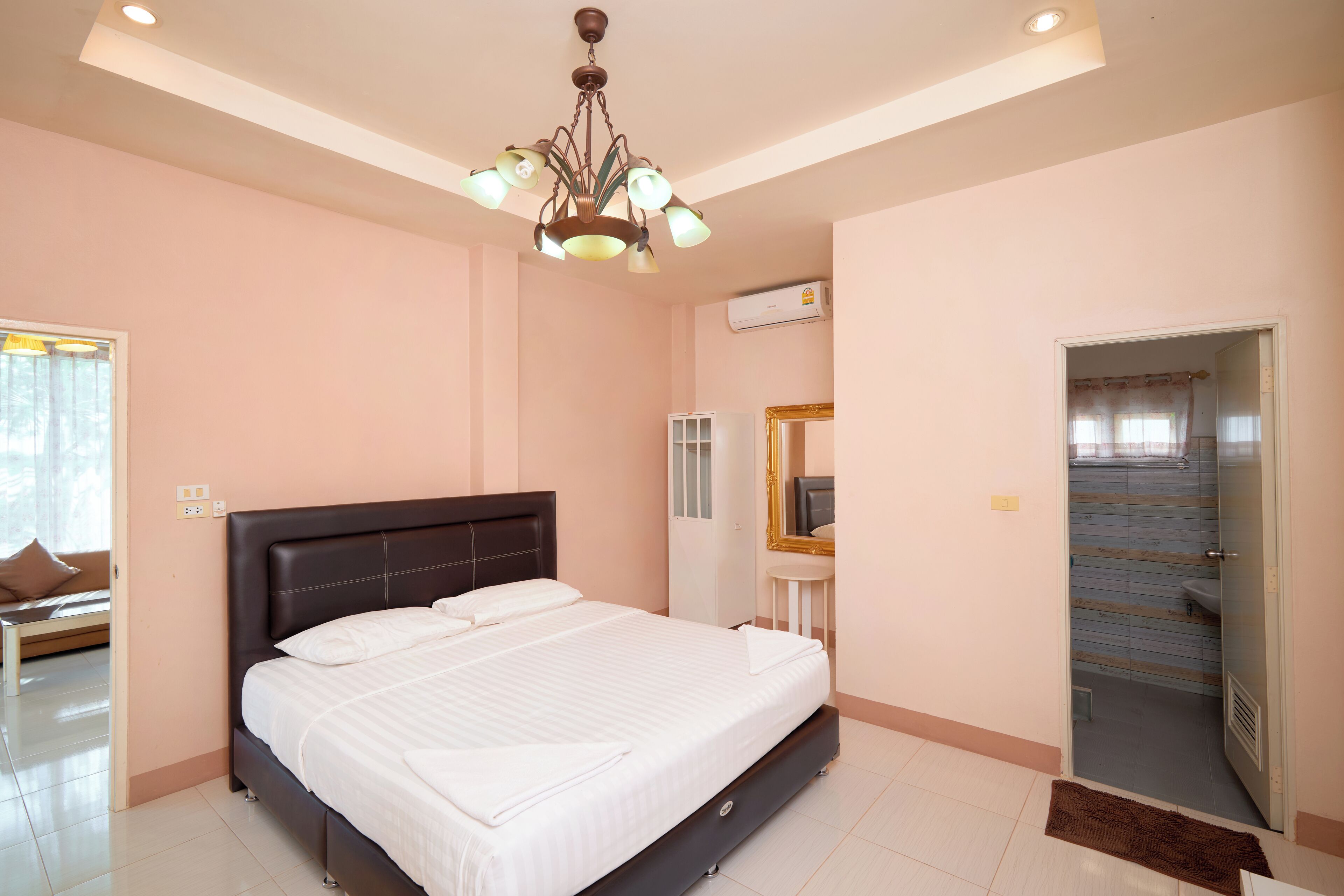 A bedroom with a large bed, a chandelier, a mirror, and a bathroom door.