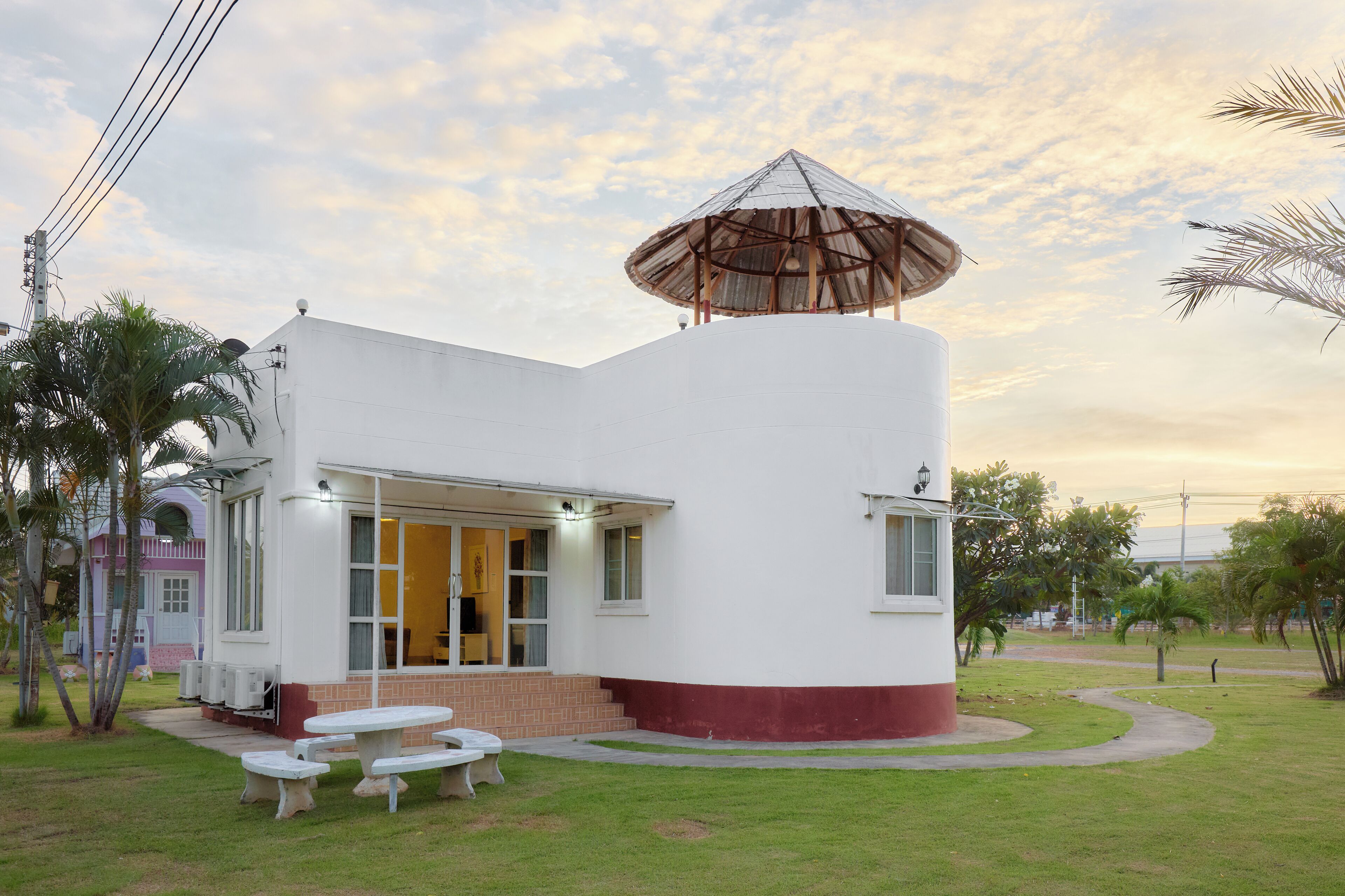 A modern white building with a large umbrella structure, a covered patio, and a small garden area with a picnic table.
