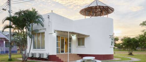 A white building with a covered outdoor seating area and a small garden.