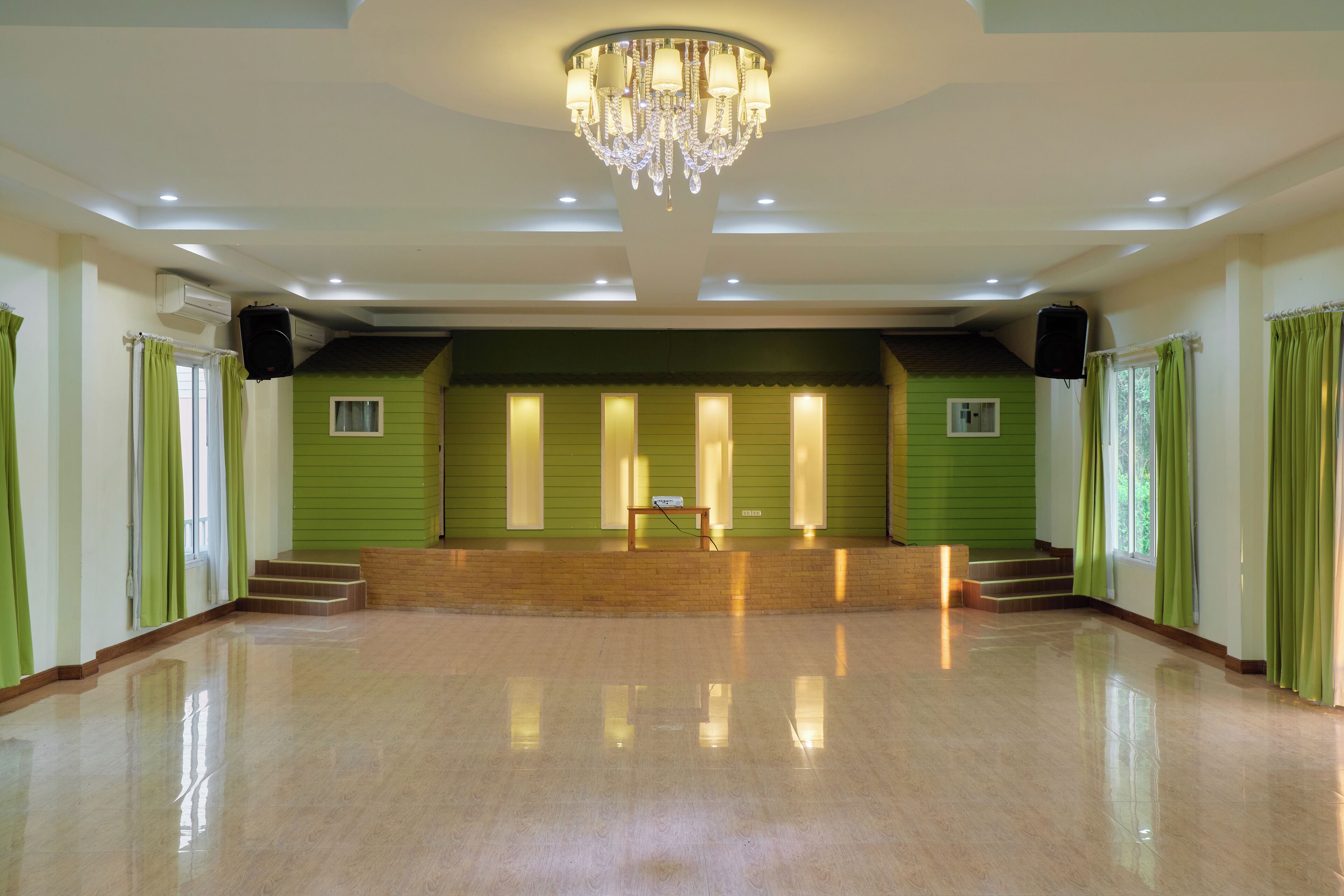 A spacious hall with a polished floor, a stage with a podium, and a chandelier.