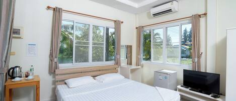 Una habitación de hotel con cama, televisor, escritorio y ventana con cortinas.