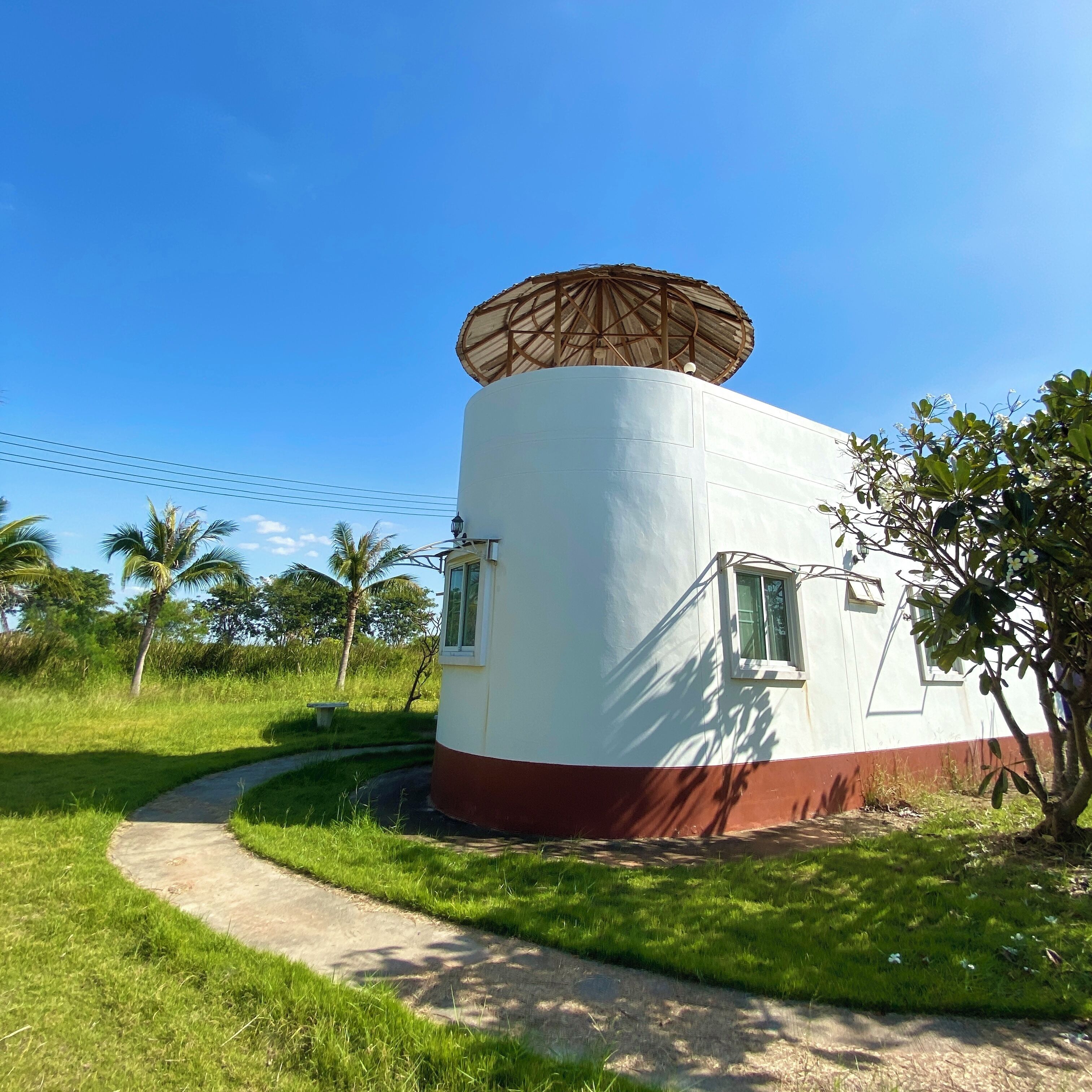 A cylindrical building with a conical roof, surrounded by greenery and a clear sky.