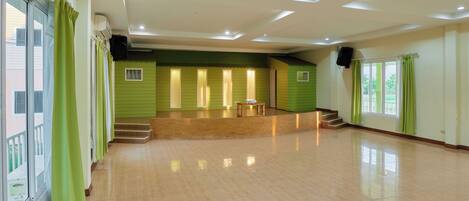 Una habitación amplia con piso de madera pulida, un escenario con una mesa y una escalera que conduce a un nivel superior.