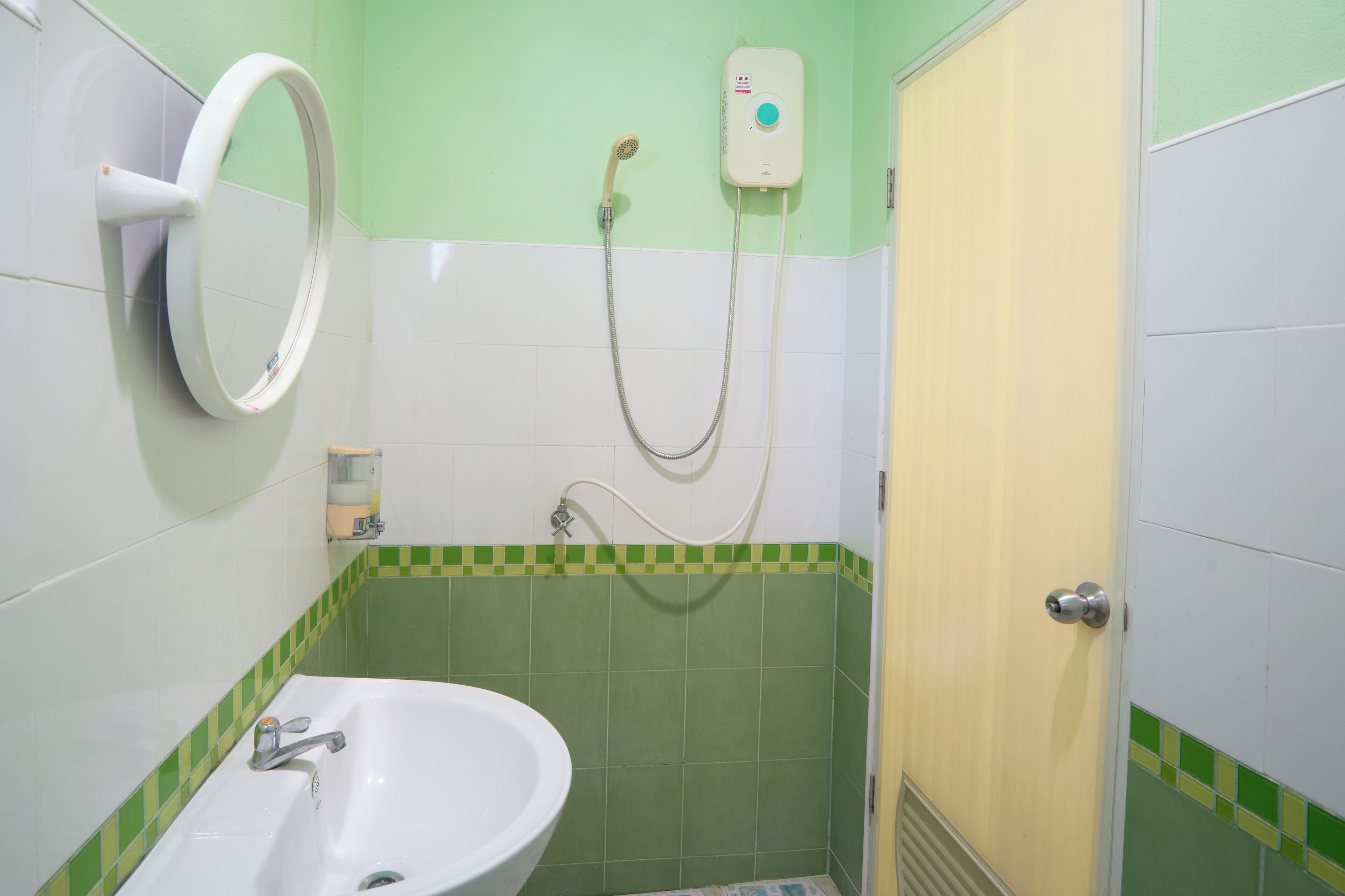 A bathroom with a sink, a mirror, a shower with a handheld showerhead, and a wall-mounted soap dispenser.