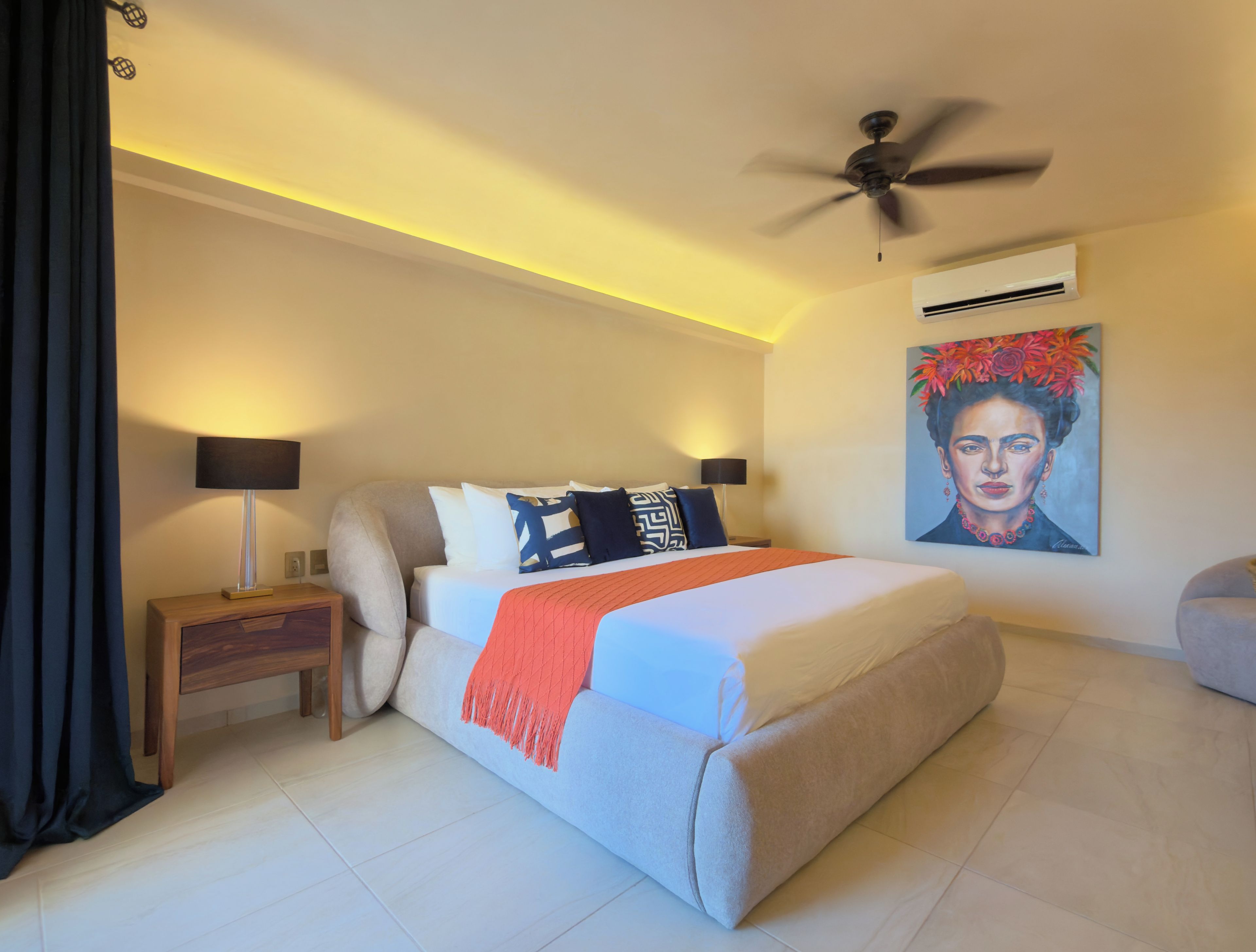 Een hotelkamer met een bed, nachtkastjes, een plafondventilator, een airconditioning en een schilderij aan de muur.