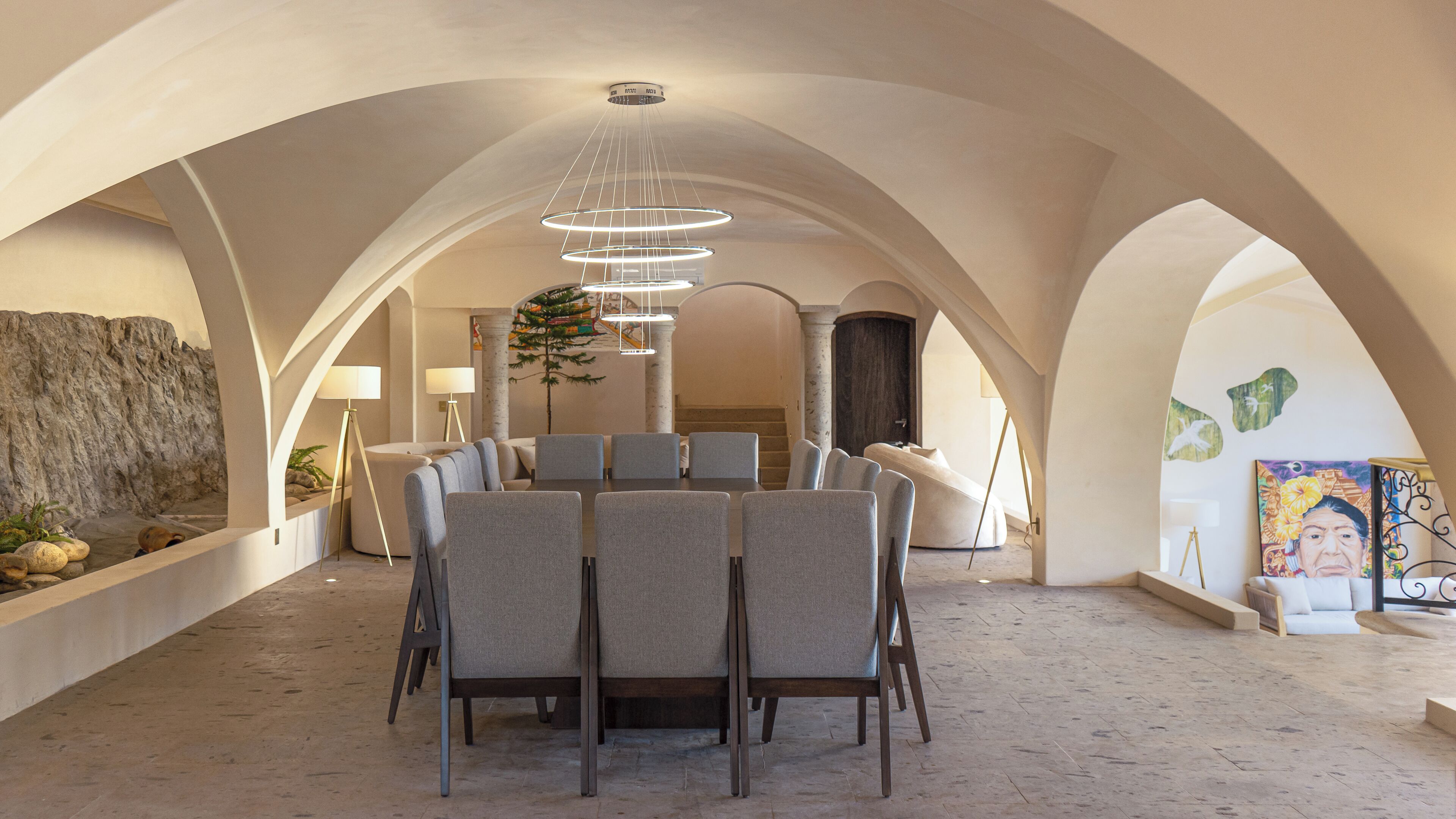 A spacious dining area with a high arched ceiling, modern furniture, and a central chandelier.