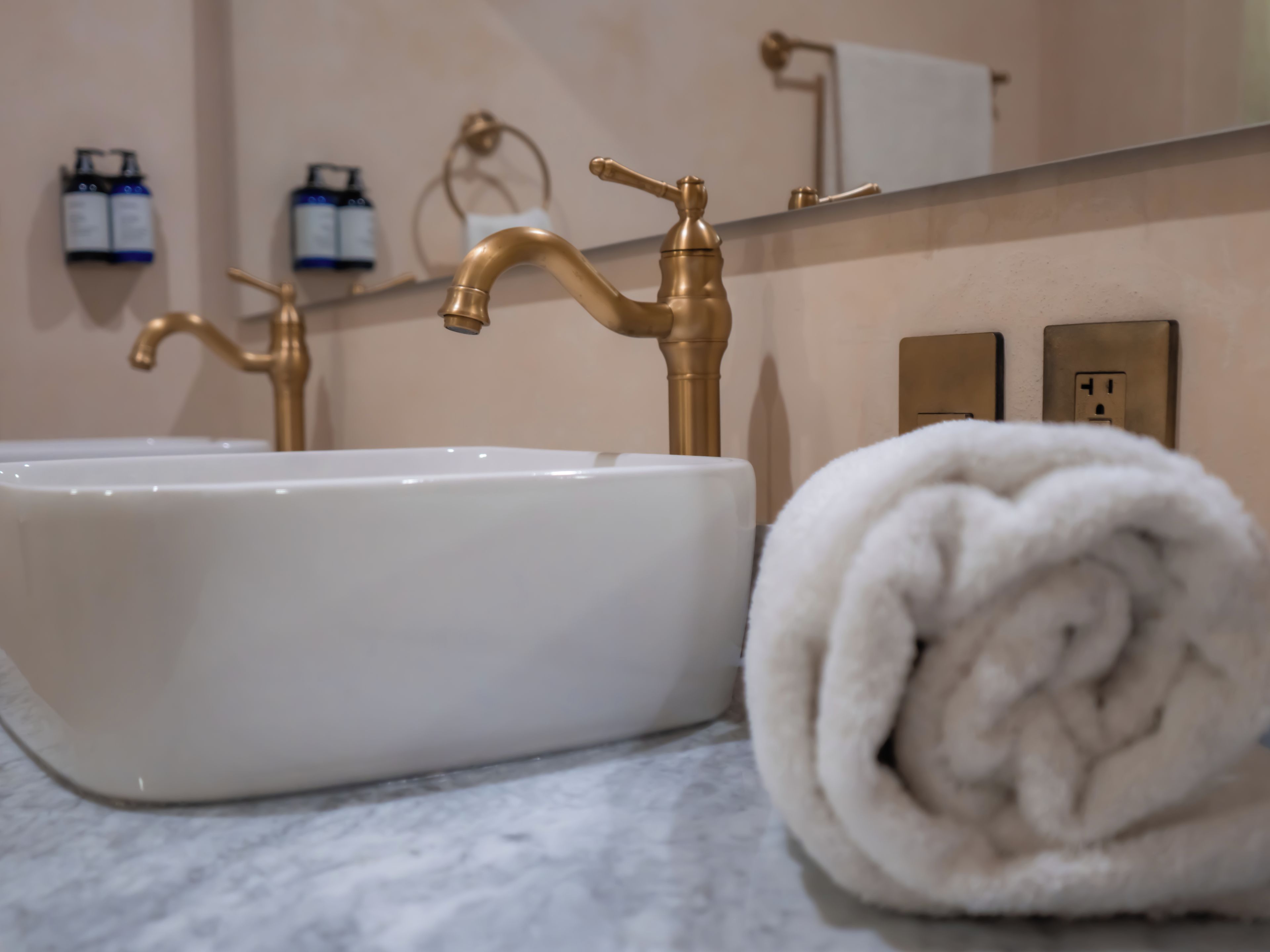 Une salle de bain avec un lavabo blanc, des robinets dorés, une serviette et un miroir.