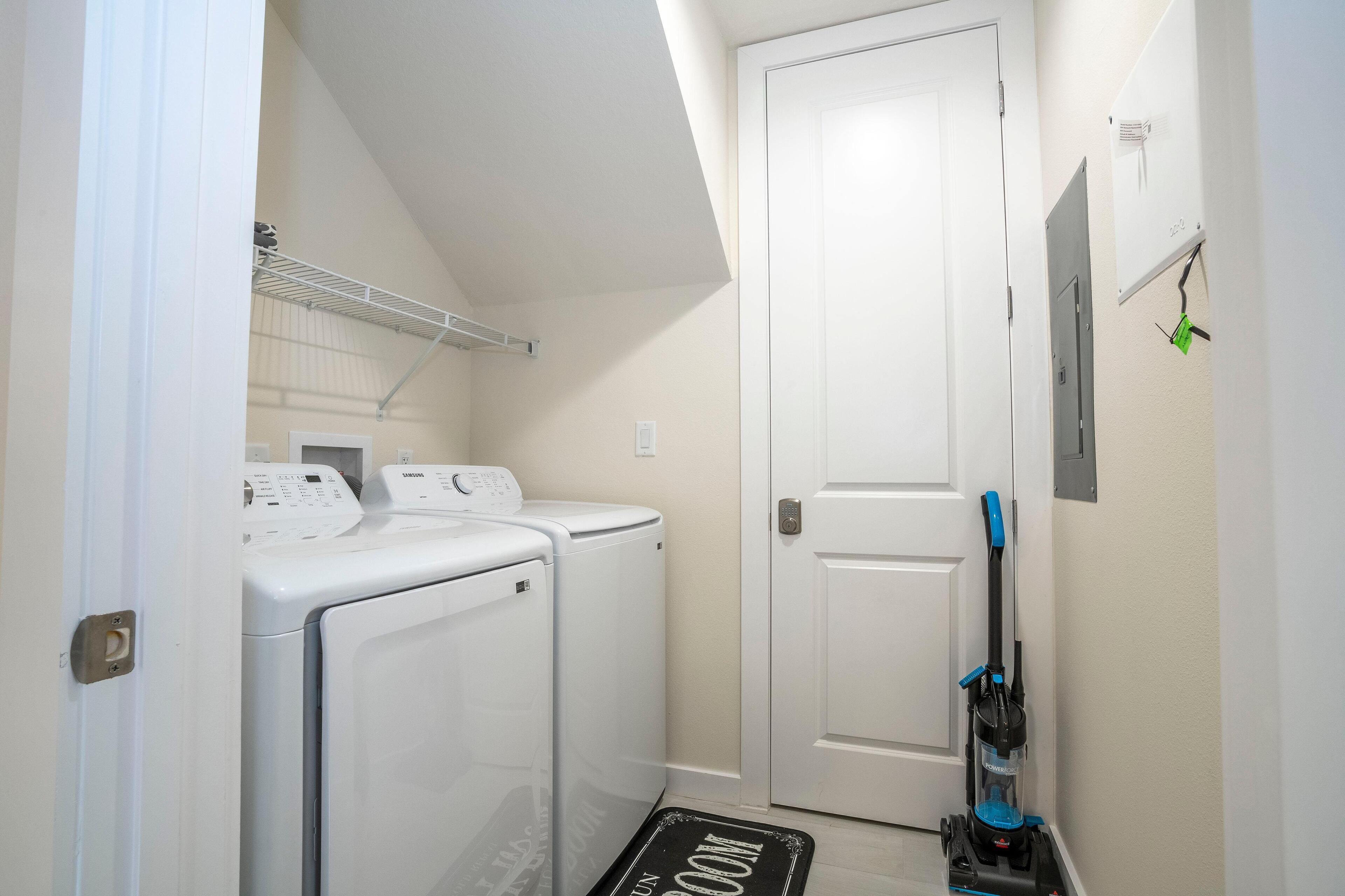 A laundry room with two front-loading washing machines, a dryer, and a vacuum cleaner.