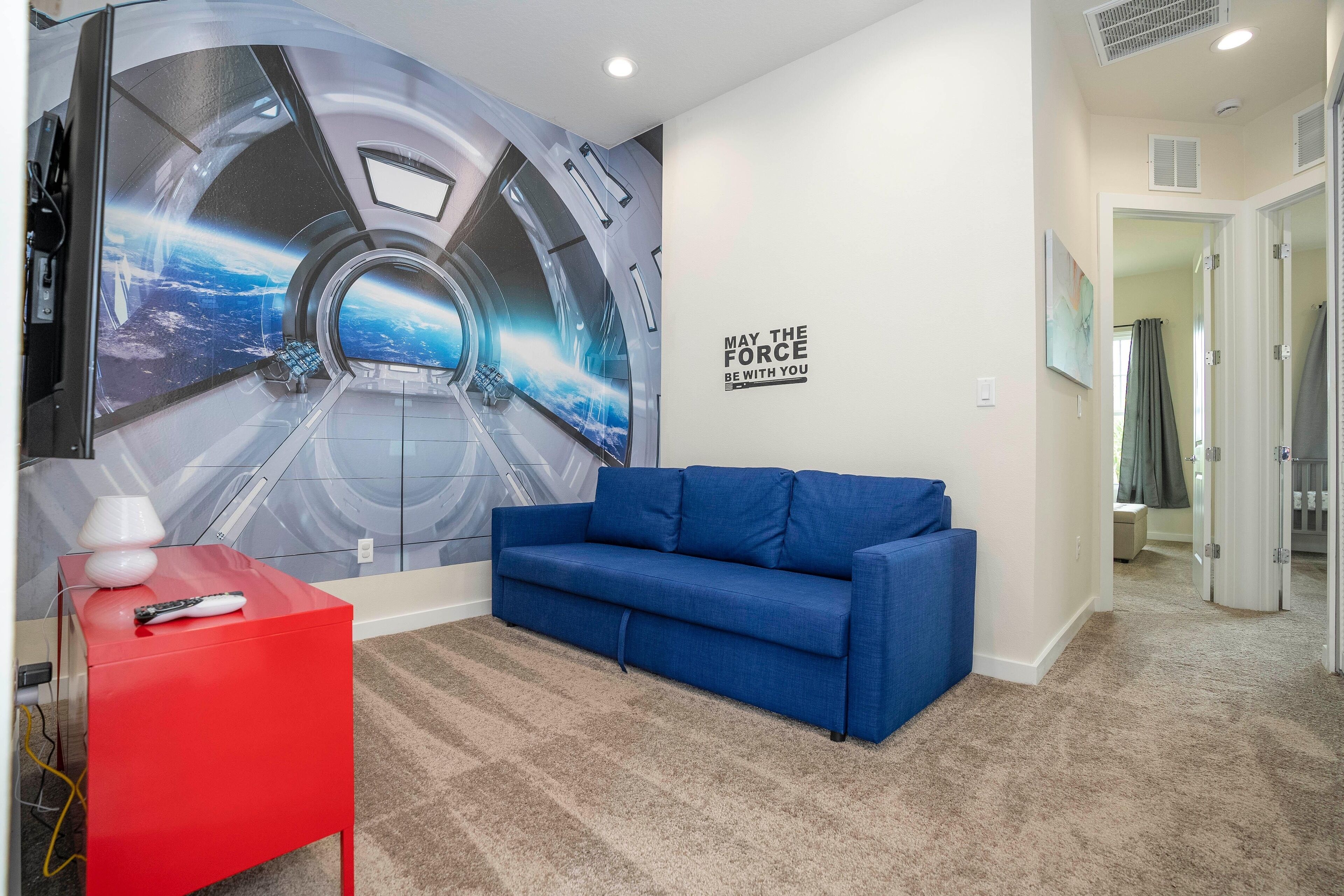 A room with a large space-themed mural, a blue sofa, a red side table, and a wall quote.