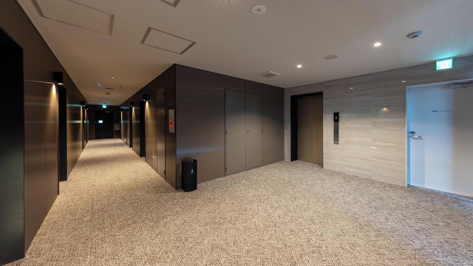Un corridoio d'hotel con pavimenti tappezzati, porte dell'ascensore e un cestino.