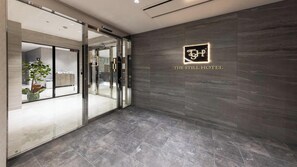 A hotel lobby with a modern design, featuring a glass entrance, a logo on the wall, and a tiled floor. - THE STILL HOTEL (Ozu)