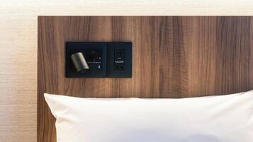 Una cama con un almohadón blanco y una mesita de noche negra con un objeto cilíndrico y un puerto USB.