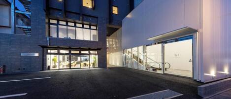Una entrada de hotel moderna con fachada de vidrio, un área de estar exterior y una escalera que conduce a un nivel superior.