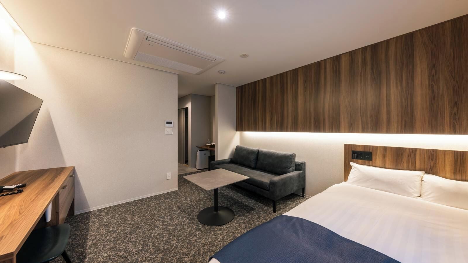 A hotel room with a bed, a desk, a sofa, a coffee table, and a TV.