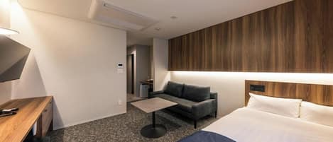 A hotel room with a bed, a desk, a sofa, a coffee table, and a TV.