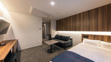 Quarto de hotel com cama, escrivaninha, sofá, mesa de centro e televisão.