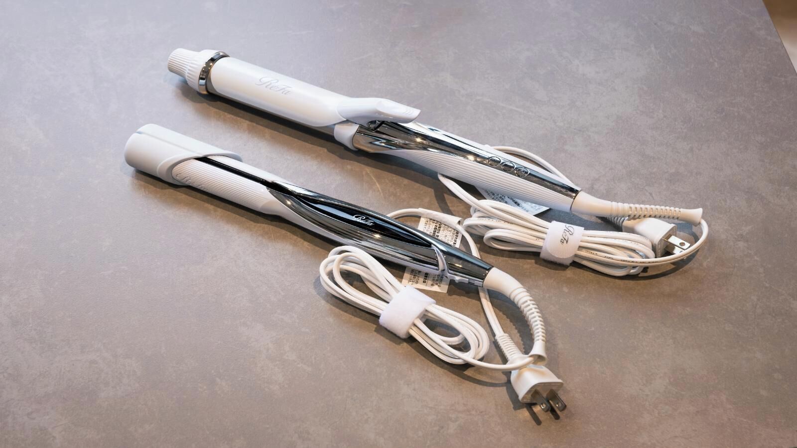 Deux appareils électroniques blancs, équipés de câbles et d’un adaptateur secteur, sont posés sur une surface texturée.