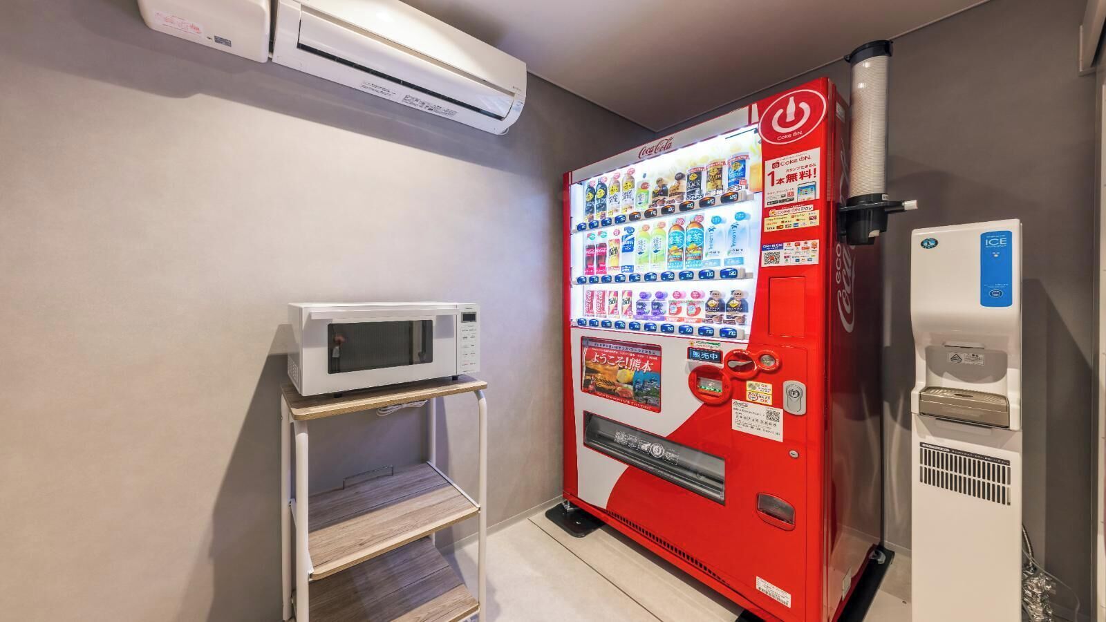 A vending machine with various drink options, a microwave, and an air conditioning unit in a room.