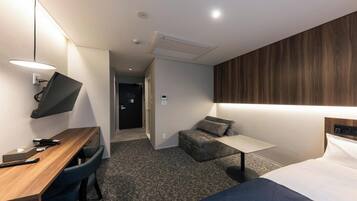 A hotel room with a desk, chair, bed, and a small sofa.