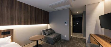 A hotel room with a bed, a small round table, a sofa, a TV, and a wooden desk.