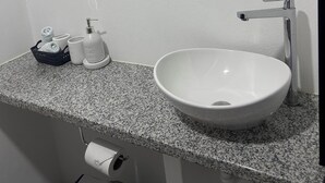 A bathroom with a granite countertop, a white sink, a round mirror, and a towel rack. - CORAL APARTMENT IN QUEPOS CLOSE TO MANUEL ANTONIO BEACH AND RESTAURANTS (Quepos)