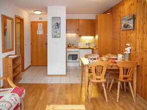 A compact kitchen with wooden cabinets, a dining table with chairs, and a small oven. - Eaux-Vives 205 by Interhome (Ovronnaz)