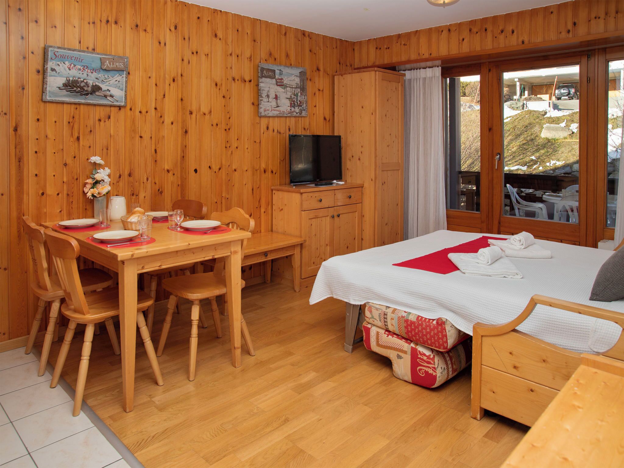 Eine Holzhütte mit Essbereich, einem Fernseher, einem Bett und Blick ins Freie.