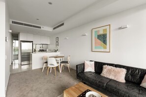 A modern living room with a black leather sofa, a wooden coffee table, and a dining area with a white table and chairs. - CBD Apartment w/ Free Parking & Gym (Melbourne)