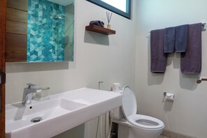 A bathroom with a white sink, a mirror, a toilet, and a towel rack with two towels. - Wave House Surf Camp Bingin (Pecatu)