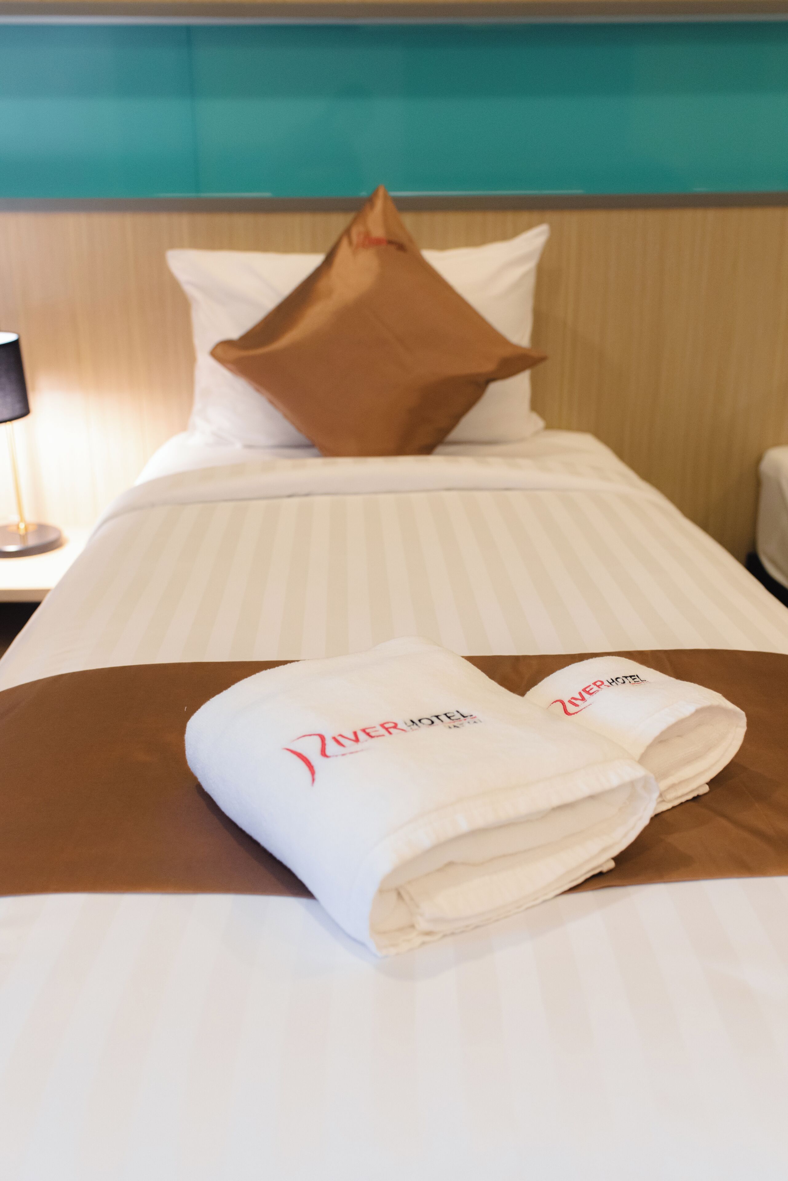 Une chambre d’hôtel avec un lit, des oreillers et une serviette pliée sur laquelle figure le nom de l’hôtel.
