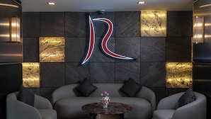 A modern lobby with a large illuminated 'R' sign, a grey sofa, and a round coffee table with flowers. - River Hotel Hatyai (Hat Yai)