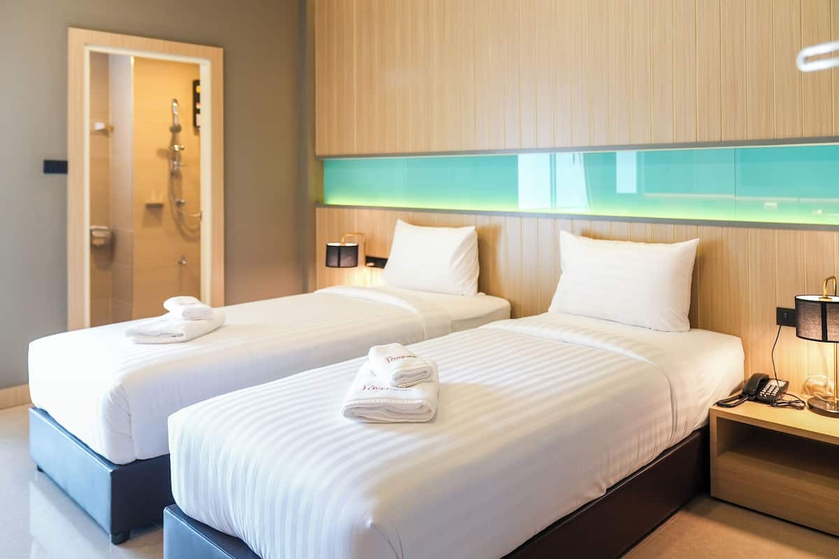 Ein Hotelzimmer mit zwei Betten, jeweils mit weißen Laken und Handtüchern, einem Holzkopfteil, Nachttischlampen und einer sichtbaren Badezimmertür.