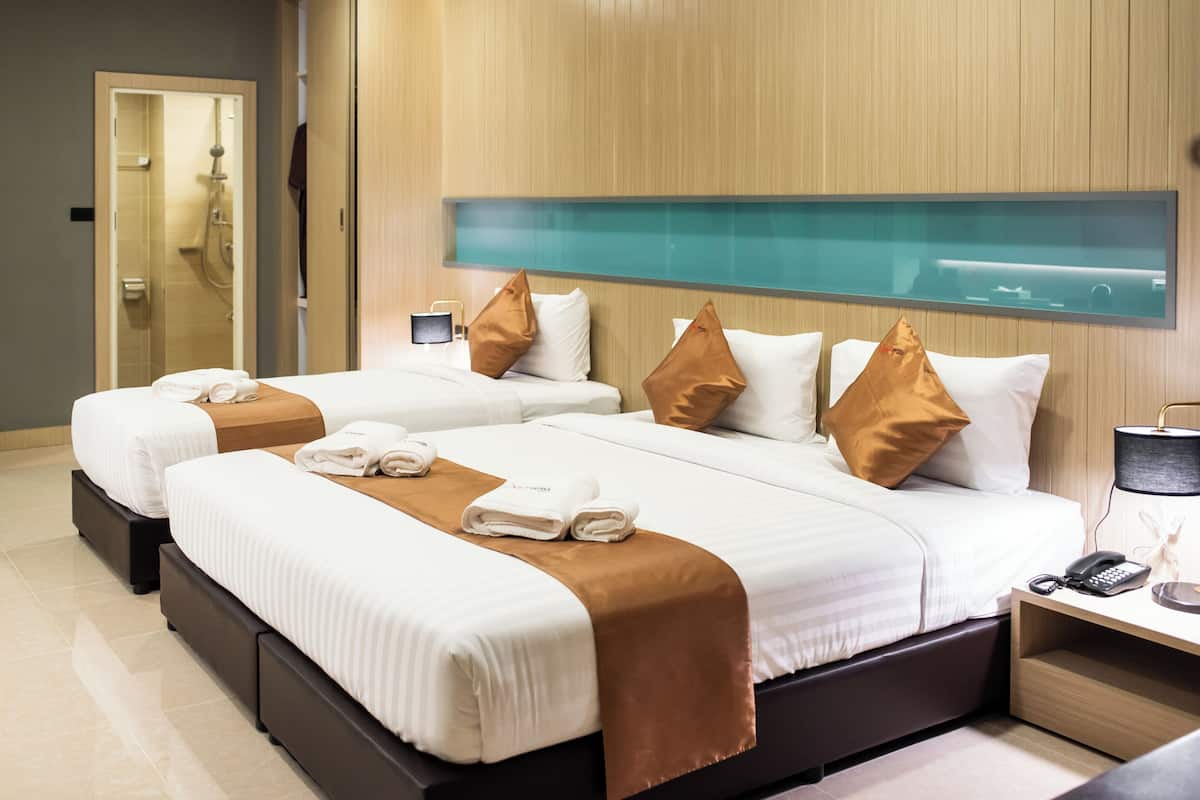 Ein Hotelzimmer mit zwei Betten, einer Duschkabine aus Glas, einem Nachttisch mit Telefon und einem wandmontierten Fernseher.