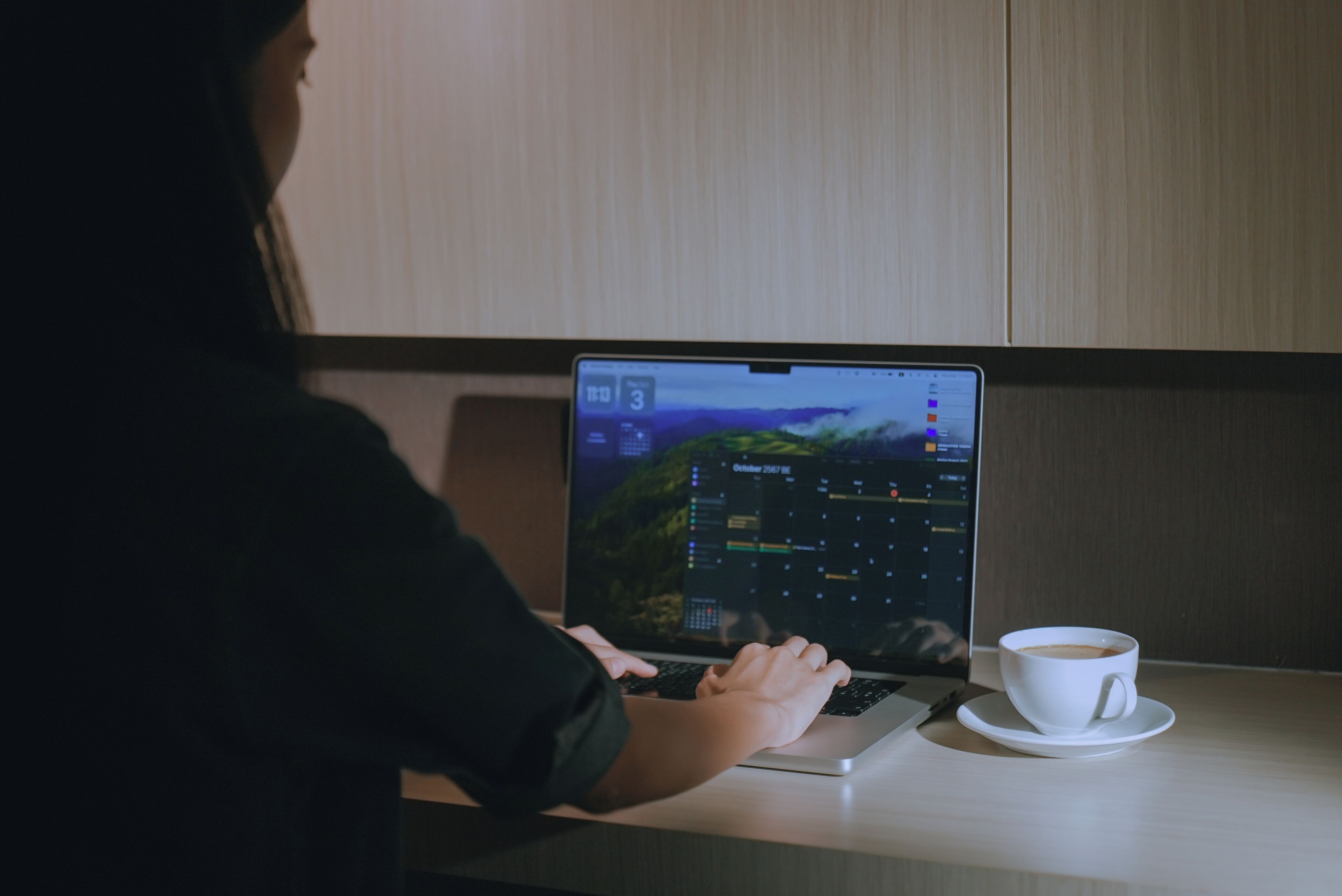 A person using a laptop on a desk with a cup of coffee.