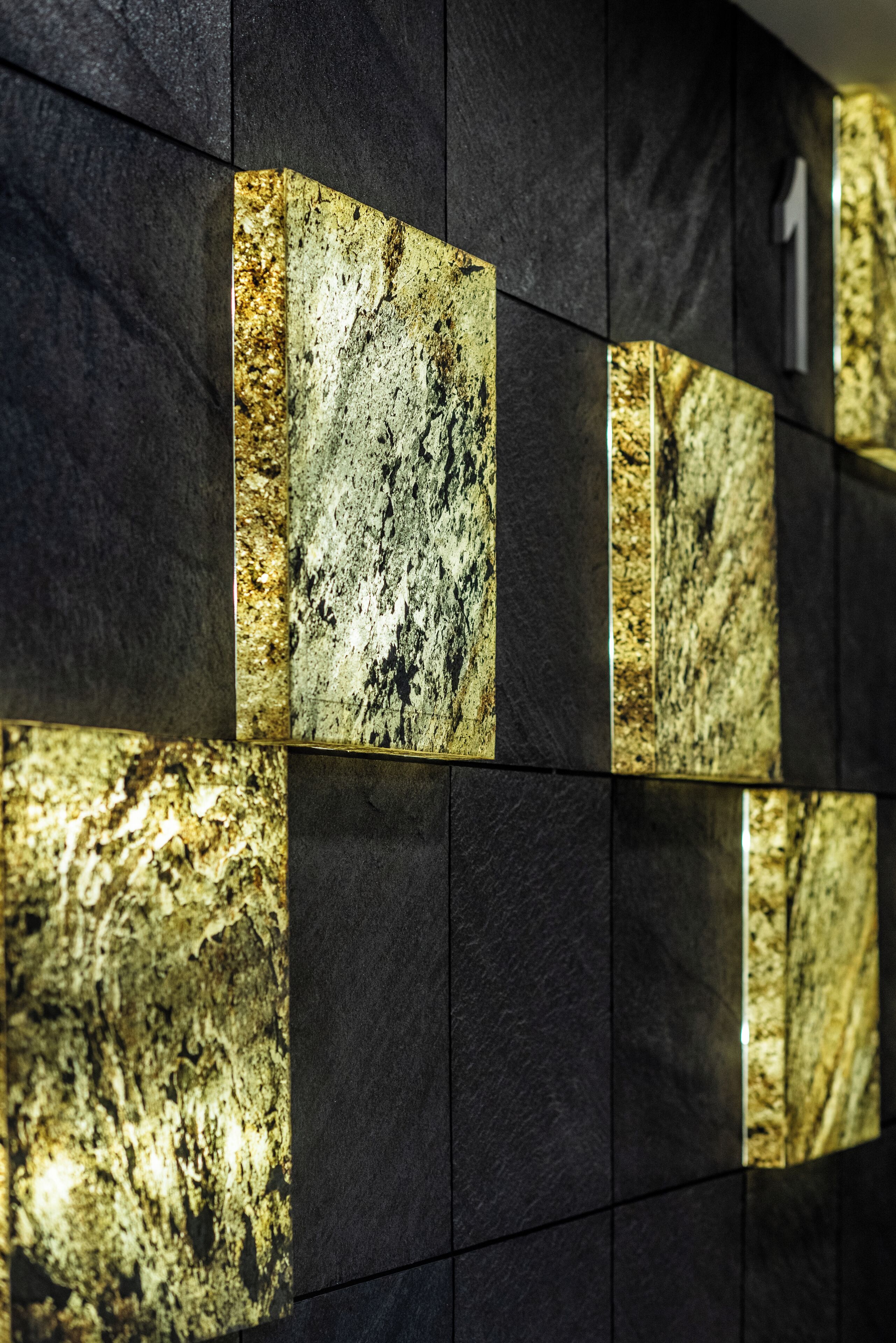 Una pared con un diseño de baldosas negras y detalles que imitan el mármol dorado.