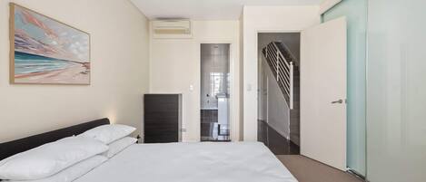 Habitación de hotel con cama, un cuadro, aire acondicionado, baño y una escalera.