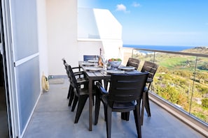 A balcony with a table set for dining, overlooking a scenic landscape. - A Sunny Bay View + shared pool Gozo, Xagħra Gozo, Malta (Xagħra Gozo)