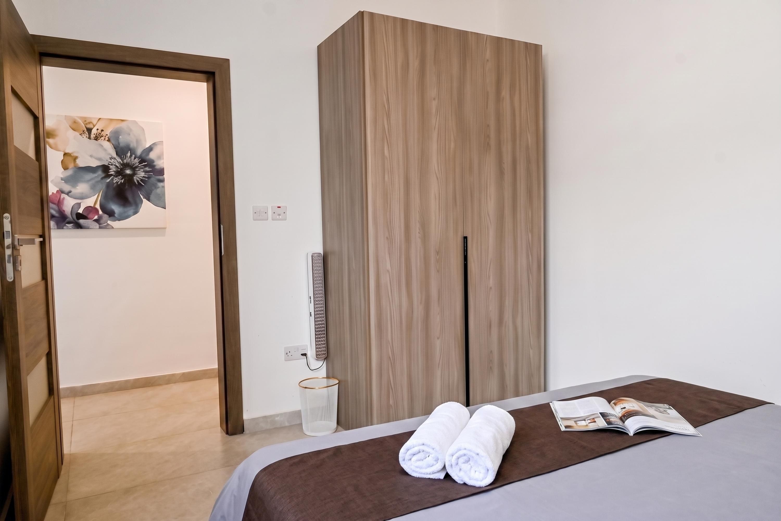A hotel room with a bed, a wooden wardrobe, a shower area, and a door leading to another room.
