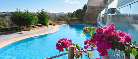 A swimming pool with clear blue water, surrounded by greenery and a stone wall.