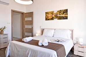 A hotel room with a bed, bedside tables, a wall-mounted picture, and a door. - A Sunny Bay View + shared pool Gozo, Xagħra Gozo, Malta (Xagħra Gozo)