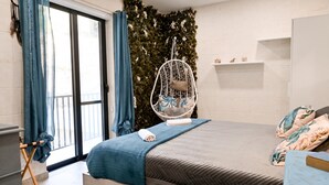 Ein Schlafzimmer mit einem Bett, einem Hängesessel, einem Fenster mit Vorhängen, einer mit Grünpflanzen bepflanzten Wand und einem kleinen Regal mit Gegenständen.