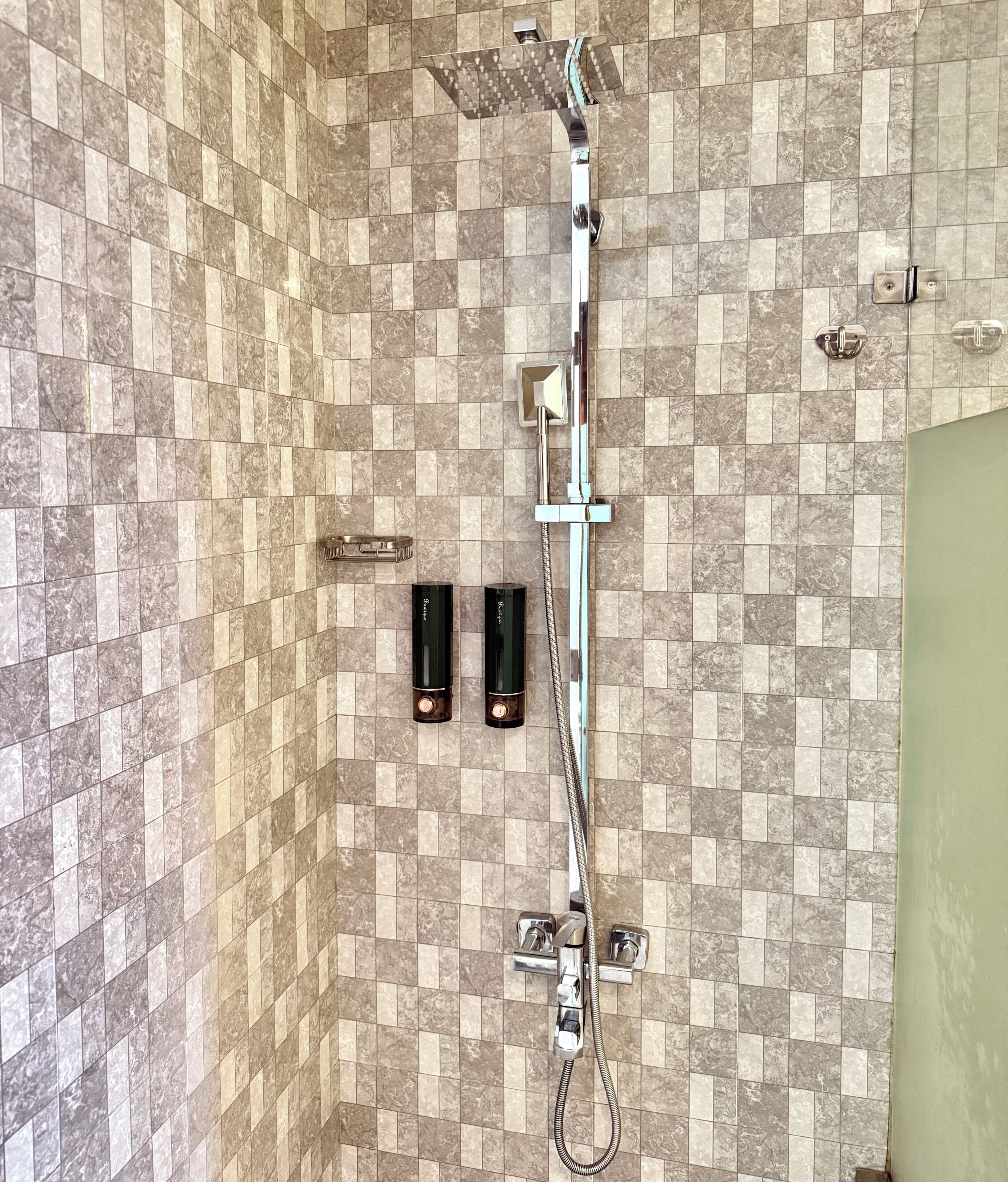 A shower with a handheld showerhead, a wall-mounted control panel, and two bottle-shaped soap dispensers.