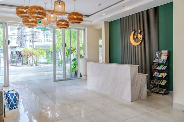 A hotel reception area with a marble reception desk, a green wall with a crescent moon decoration, and a magazine rack.
