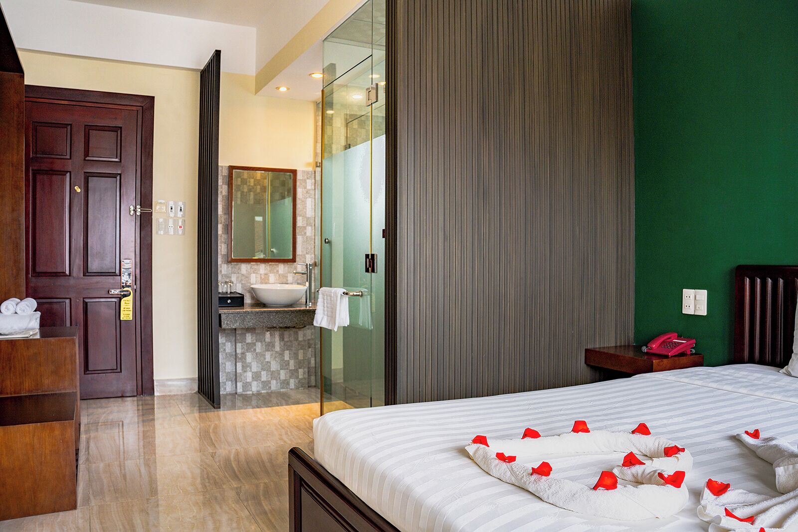 A hotel room with a bed, a wooden dresser, a bathroom with a sink and mirror, and a green wall.