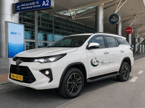A white SUV parked in front of an airport terminal with signs for Vietnam Airlines and Vietnam Air. - Horizon Hotel by LunaVerde Hoi An (Thanh pho Hoi An)